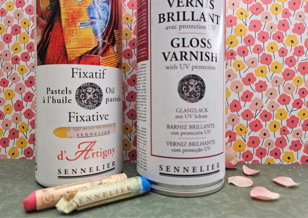 Two Sennelier art product bottles labeled Fixatif and Gloss Varnish with UV protection sit in front of a pink floral wallpaper, with pastel sticks on the counter.