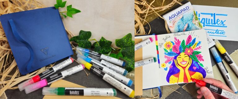 Blue notebook with a blue ribbon, surrounded by colorful markers and green ivy on a straw background; art supplies scene
