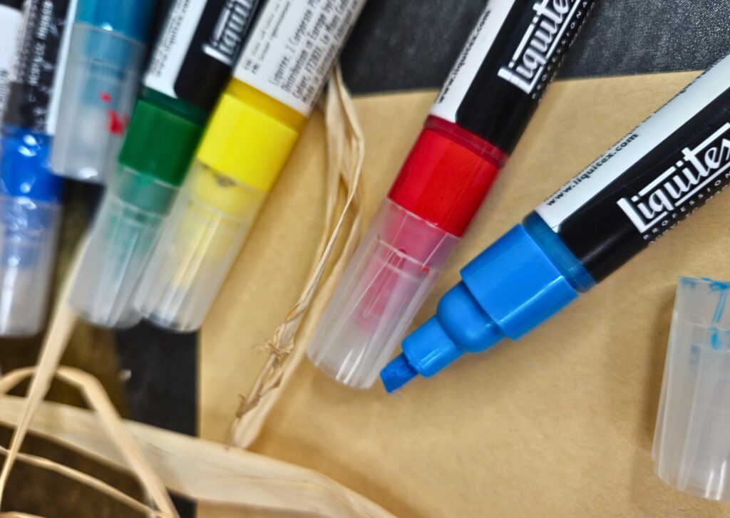 Close-up of colorful marker pens and caps laid out on a wooden surface, blue, red, yellow hues visible.