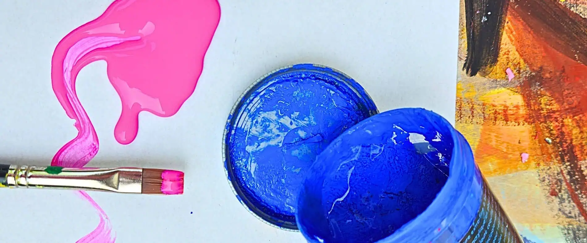 acrylique peinture artiste peintre atelier conseils Pink paint spilling from a brush beside an open blue paint can on a light background with a canvas edge nearby.