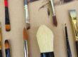 Assorted paintbrushes laid out on a brown cardboard surface.