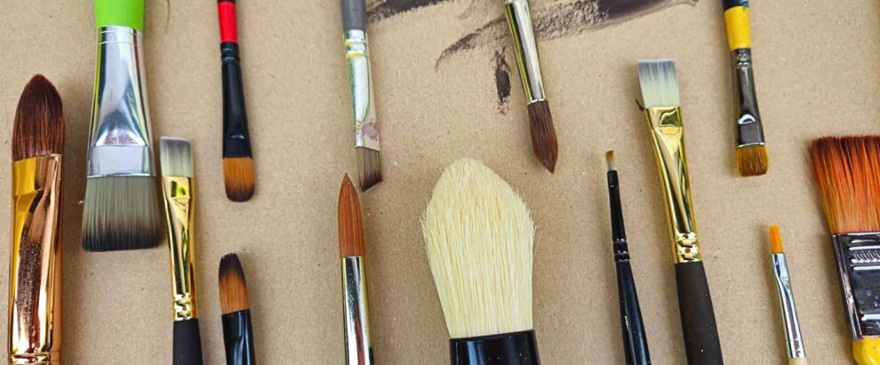 Assorted paintbrushes laid out on a brown cardboard surface.