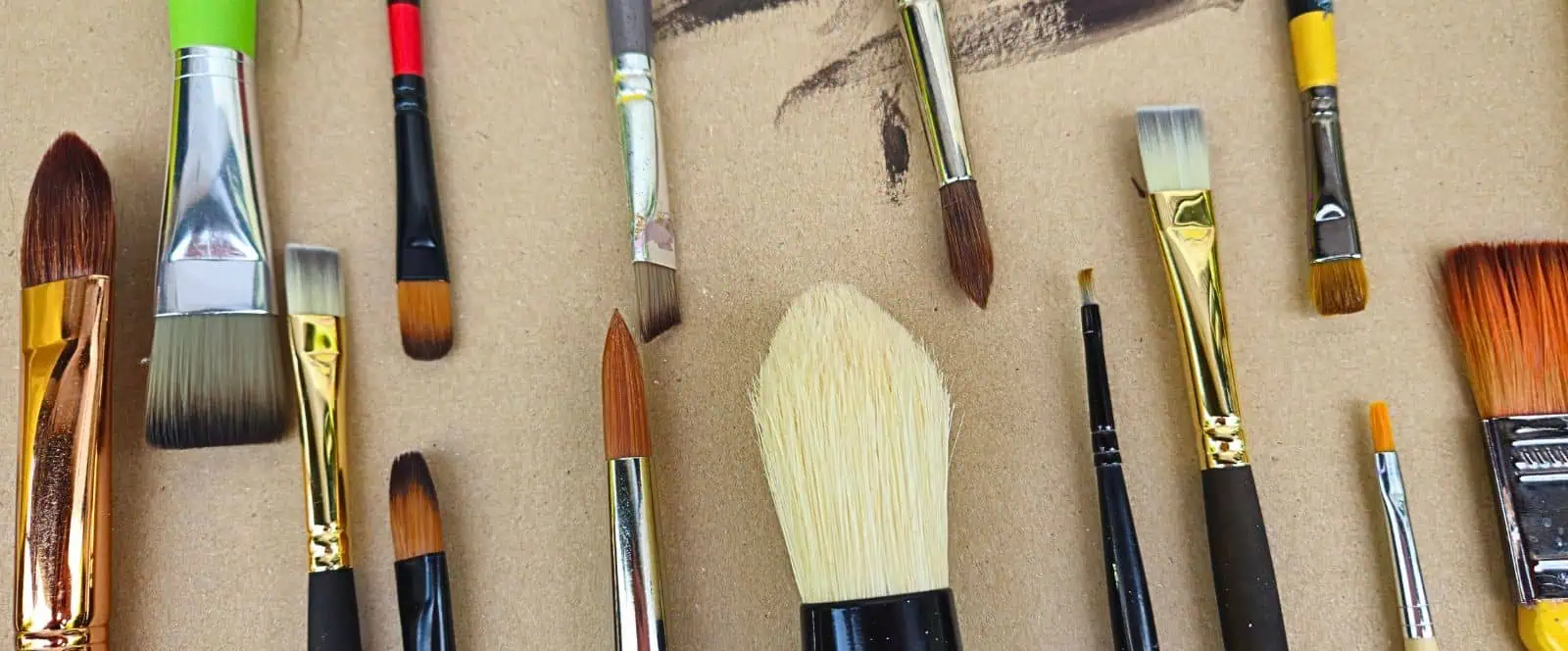 pinceaux conseils comprendre l’anatomie du matériel Assorted paintbrushes laid out on a brown cardboard surface.