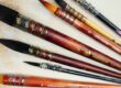 Set of colorful paintbrushes with wooden handles lying on a textured art canvas surface, ready for painting