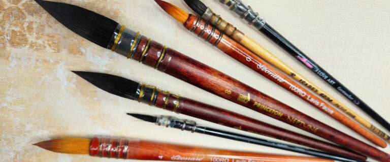 Set of colorful paintbrushes with wooden handles lying on a textured art canvas surface, ready for painting