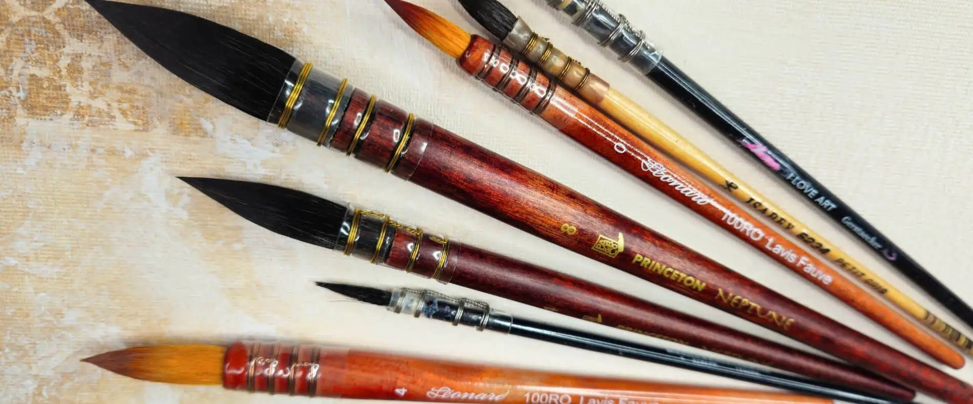 Set of colorful paintbrushes with wooden handles lying on a textured art canvas surface, ready for painting